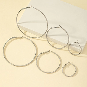 Three pairs of polished silver hoop earrings in varying sizes on a minimalist display