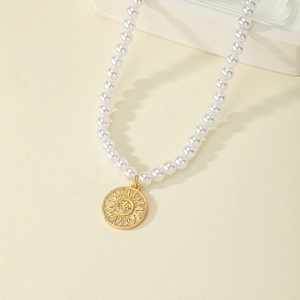 Elegante collana di perle con ciondolo a moneta sole dorata su sfondo neutro