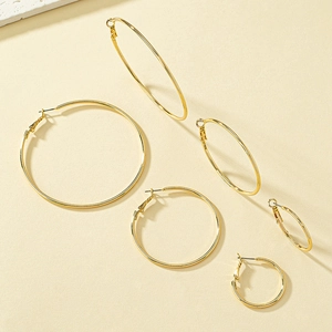 Three pairs of golden hoop earrings in different sizes on a textured beige background