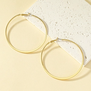 Polished gold large hoop earrings with textured sawtooth pattern on a stone pedestal