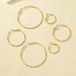 Three pairs of classic minimalist gold hoop earrings in various sizes on sandy background