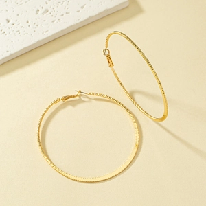 Detailed close-up of large gold hoop earrings with intricate textured ripple pattern