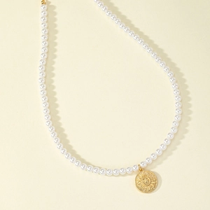 Collana di perle minimalista con ciondolo a sole dorato su sfondo beige chiaro