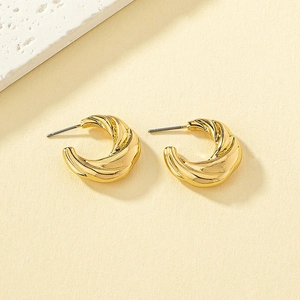 Detailed view of gold twisted C-shape hoop earrings with spiral texture on stone background