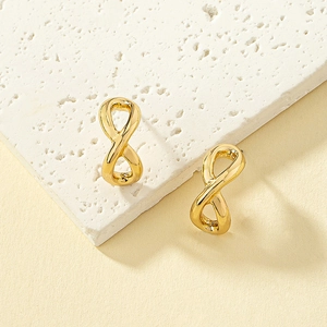 Gros plan de boucles d'oreilles dorées symbole infini sur une plaque de marbre blanc