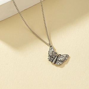 Vintage silver butterfly pendant necklace with intricate wing texture on a beige background