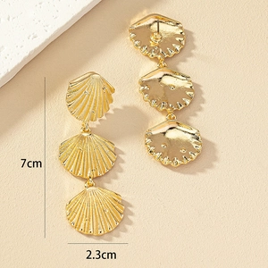Three-tier gold shell drop earrings featuring radiating texture and 7cm length on beige background