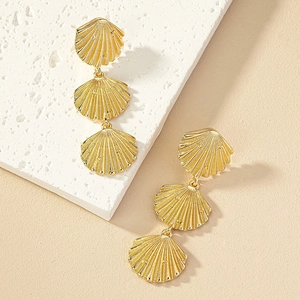 Bohemian gold triple tiered shell drop earrings on a textured minimalist stone background