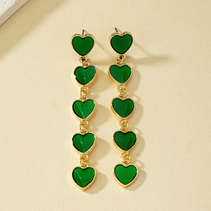 Detail of long gold dangling earrings with five green enamel hearts in a vertical row