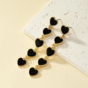 Detail view of long heart earrings featuring five black enamel charms in gold settings
