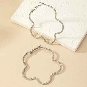 Gros plan de boucles d'oreilles fleur argentées ondulées avec texture métal martelé sur pierre