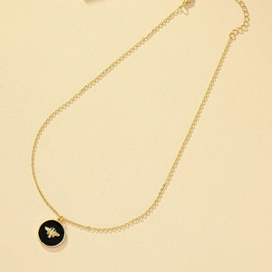 Golden enamel coin necklace featuring a 3D bee pendant on a textured beige stone background