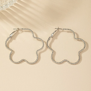 Boucles d'oreilles créoles fleurs argentées avec texture en relief et ombre artistique