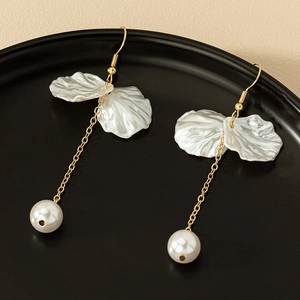 Boucles d'oreilles fleurs et perles avec pétales blancs et chaînes dorées sur plateau noir