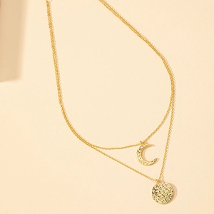 Double layered gold necklace with hammered coin and crescent moon pendants on beige background