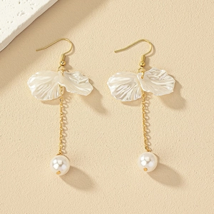 Détail de boucles d'oreilles dorées avec pétales blancs, glands et perles pendantes