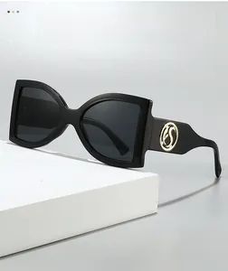 Détail de lunettes papillon avec logo S doré sur un support d'affichage blanc