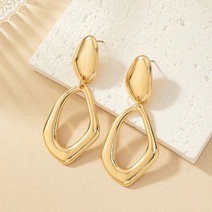 Detailed close-up of golden geometric hollow dangle earrings on a neutral warm background