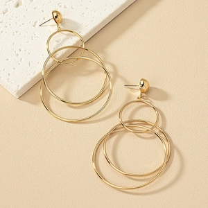 Three-layer gold geometric hoop earrings displayed on a minimalist textured surface