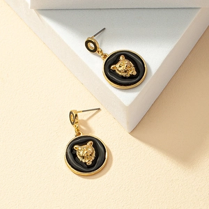 Golden lion head earrings with black enamel round pendant on a geometric stone display