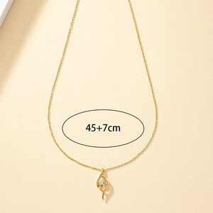 Collier en or avec pendentif courbe en S et zircon blanc sur fond beige neutre