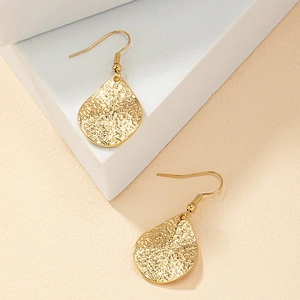 Minimalist gold teardrop earrings with hammered texture displayed on white geometric steps
