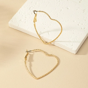 Close-up of golden heart hoop earrings with textured finish on white stone display