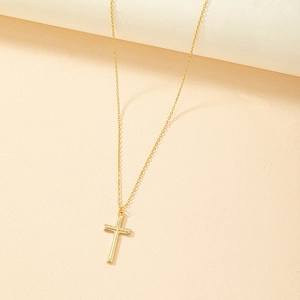 Collana con croce dorata minimalista e pendente testurizzato su sfondo color albicocca
