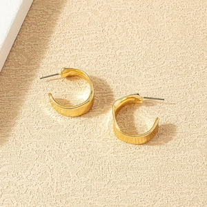 Minimalist gold-plated alloy C-shaped chunky hoop earrings on a textured beige background