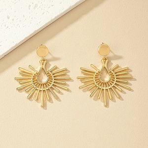 Exaggerated gold alloy sunburst earrings with radiant drops on a beige stone background