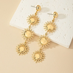 Detail of layered sunburst drop earrings in polished gold finish on a textured background