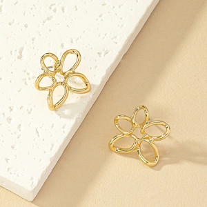 Elegant gold alloy hollow flower stud earrings displayed on white textured stone pedestal