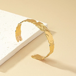 Dettaglio di un bracciale a fascia dorato con trama martellata e bordi irregolari