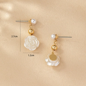 Detail shot of white camellia drop earrings with pearl and golden ball accents