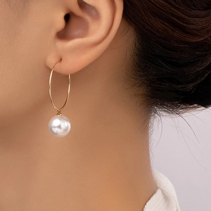 Élégantes créoles dorées avec un grand pendentif en perle blanche portées par un mannequin