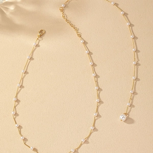 Élégant collier de perles dorées avec un grand pendentif goutte sur surface texturée