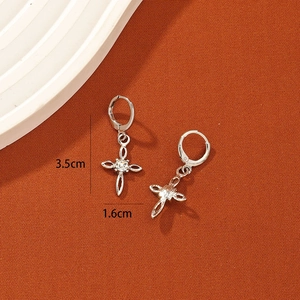 Silver cross earrings with clear zircon stones displayed on a textured warm background