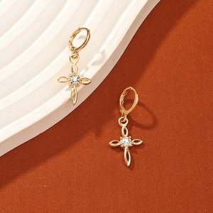 Macro detail of gold-plated huggie earrings with a sparkling zircon set in a cross charm