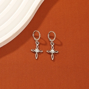 Silver cross drop earrings with clear gemstone center on textured orange background