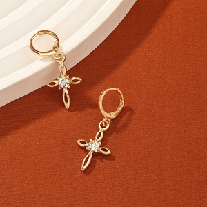 Minimalist gold cross drop earrings with clear gemstone on a warm textured background