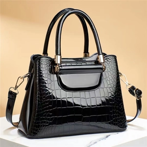 Detail of black glossy crocodile pattern tote with gold metal lock and leather strap