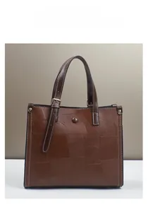 Detail of dark brown leather tote featuring geometric texture and gold metal hardware