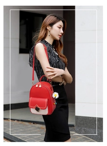 Mini red backpack with white pocket and daisy charm worn by a model on one shoulder