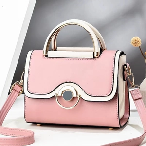 Detail of a pink and cream crossbody bag featuring a curved metal handle and gold clasp