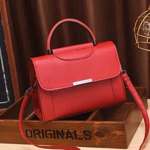 Minimalist red leather handbag with silver clasp on a vintage wood display box