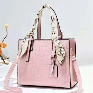 Borsa a mano rosa effetto coccodrillo con foulard decorativo e tracolla su espositore bianco