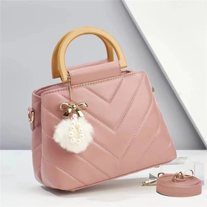 Pink quilted leather handbag with wooden top handle and decorative faux fur pompom charm