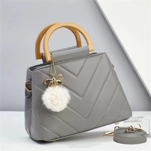 Detail of grey quilted tote bag with wooden handle, plush pom-pom and adjustable strap