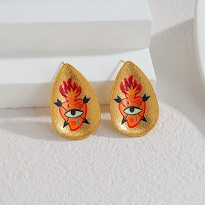 Boucles d'oreilles dorées en forme de larme avec motif cœur sacré sur socle blanc
