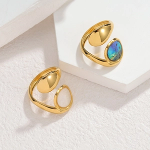 Dettaglio di anelli dorati irregolari con inserti di conchiglia su una base bianca